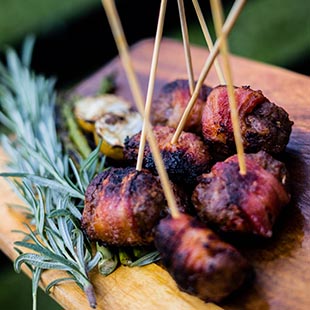 wood board with appetizers of bacon wrapped meat with a sprig of rosemary as a garnish