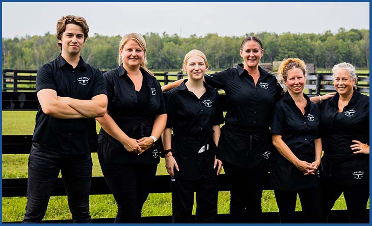 picture of Big Grill Catering Staff dressed in all black, standing in front of a farm fence and fields behind.